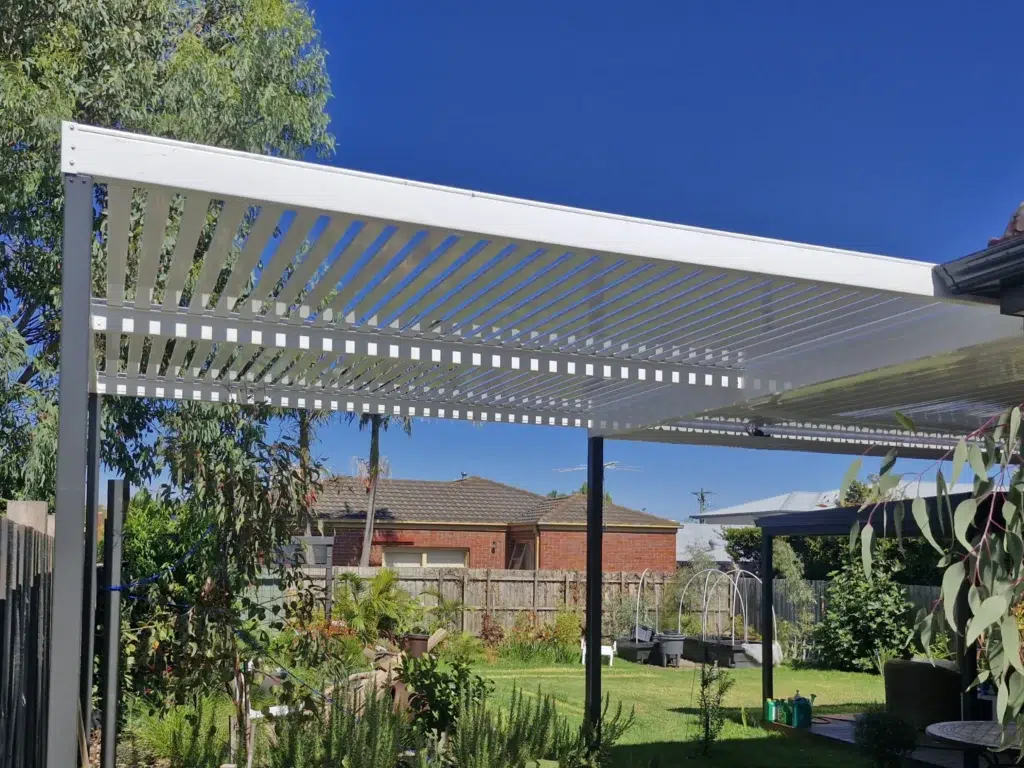 White louvred pergola with open louvres in residential backyard with lawn and established trees, Carnegie Victoria