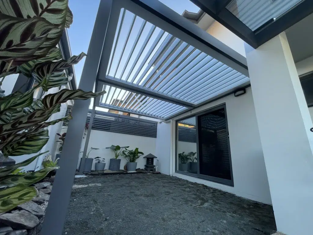 Close-up of open grey louvred pergola structure with tropical plants and modern home exterior, Pelican Waters Queensland