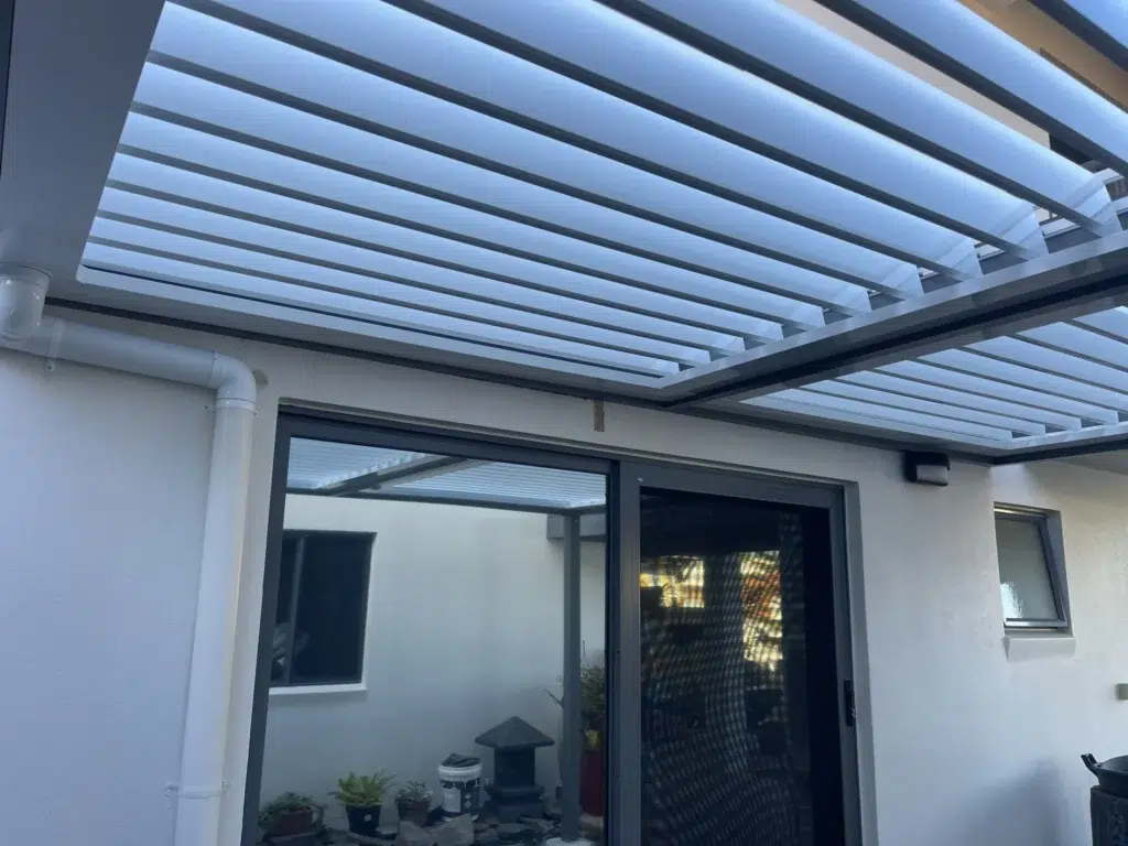 Side view of grey-frame louvred pergola with open louvres attached to white rendered home, Pelican Waters Queensland