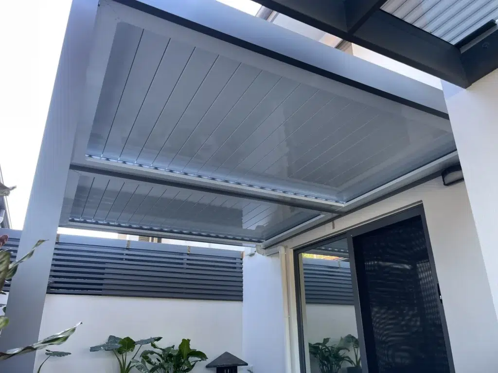 Under-structure view of open grey louvred patio with tropical foliage, Pelican Waters Queensland