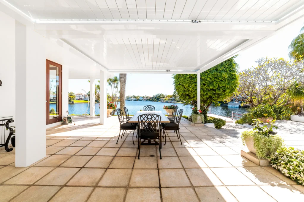 White louvred patio with closed insulated roof overlooking waterway, outdoor dining table and garden, Queensland