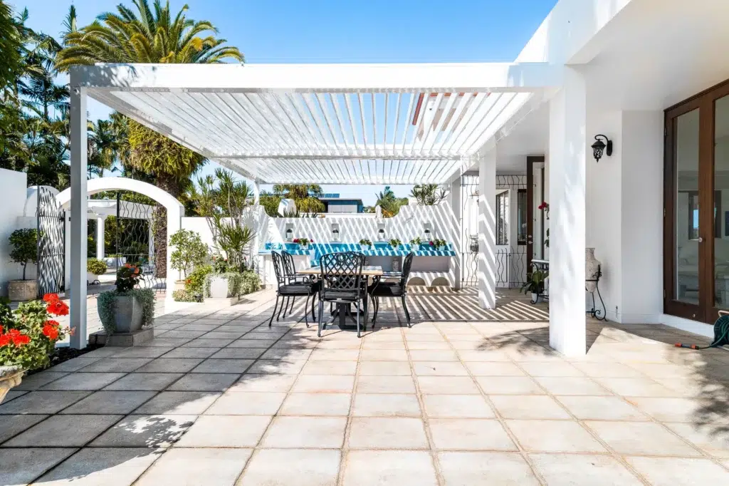 Creating the Ultimate Low-Maintenance Outdoor Entertaining Area 1 White louvred patio with open louvres and black outdoor dining chairs amid lush tropical garden, Queensland