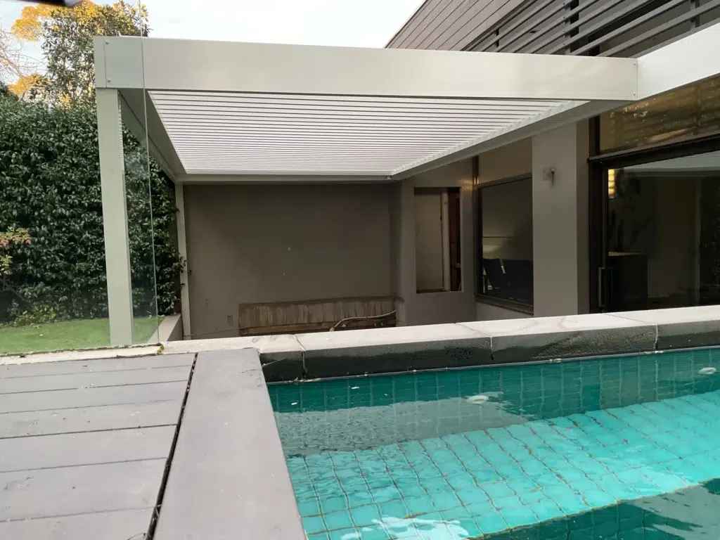 Wide view of white louvred pergola over grey paving with formal hedged garden, Glen Iris Victoria