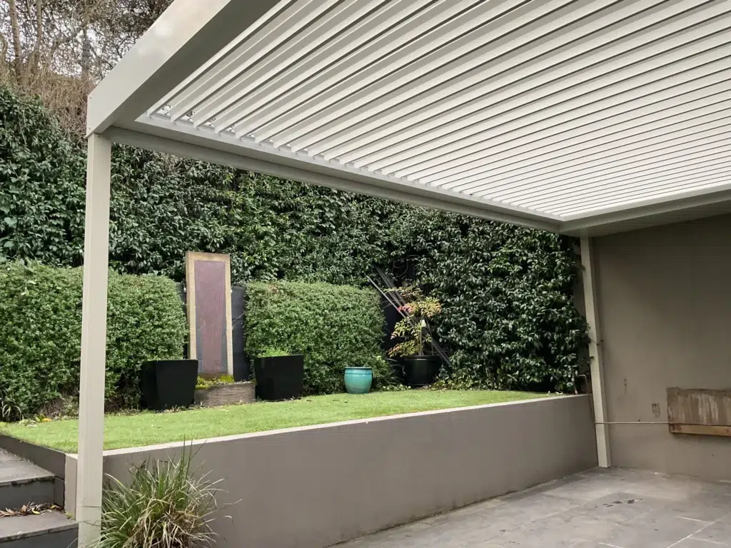 Louvred pergola with open louvres beside lush green hedge garden and landscaped patio, Glen Iris Victoria