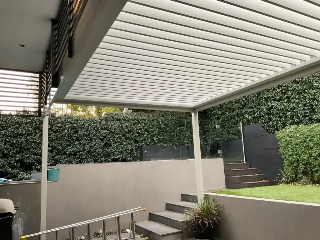 Side angle view of white louvred pergola structure with garden artwork and boxwood hedge, Glen Iris Victoria