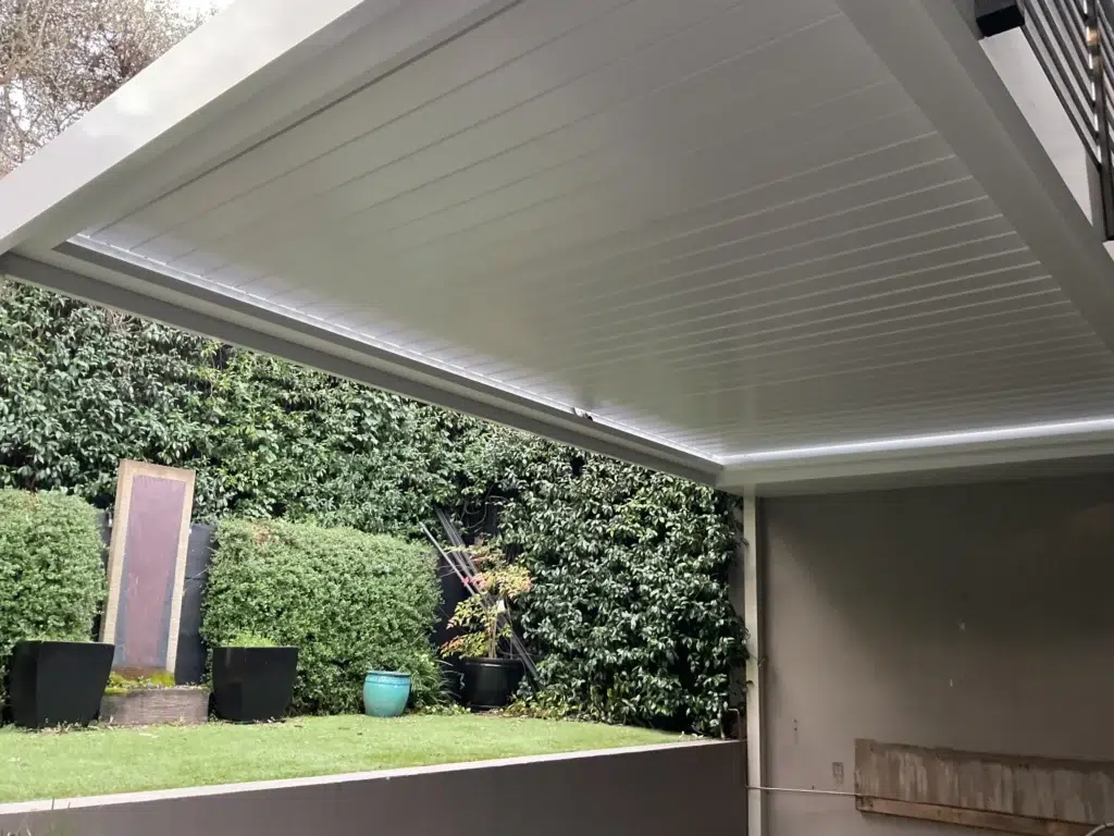 Close interior view of white louvred pergola roof panels against green foliage backdrop, Glen Iris Victoria