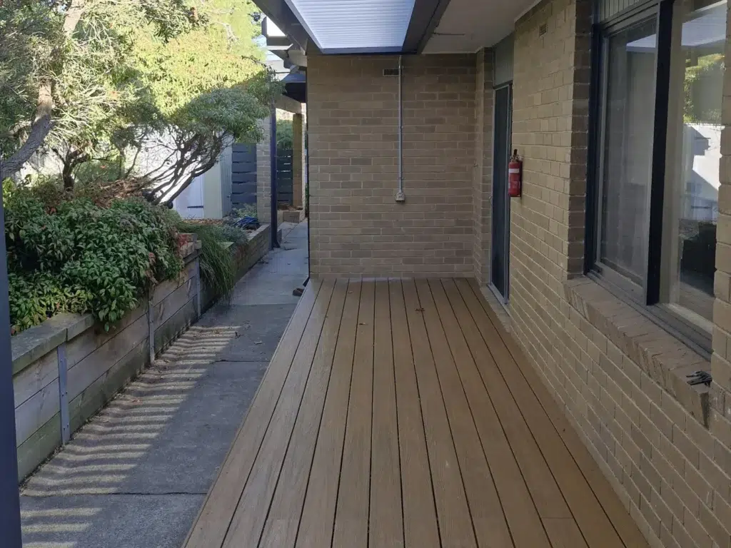 Side view of louvred roof verandah with timber deck alongside brick home and garden path, Victoria