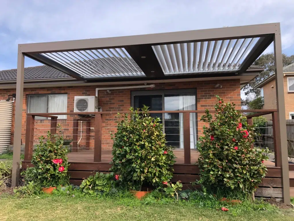 Louvred verandah with open aluminium louvres over timber deck attached to brick home with camellia bushes, Glen Waverley Victoria