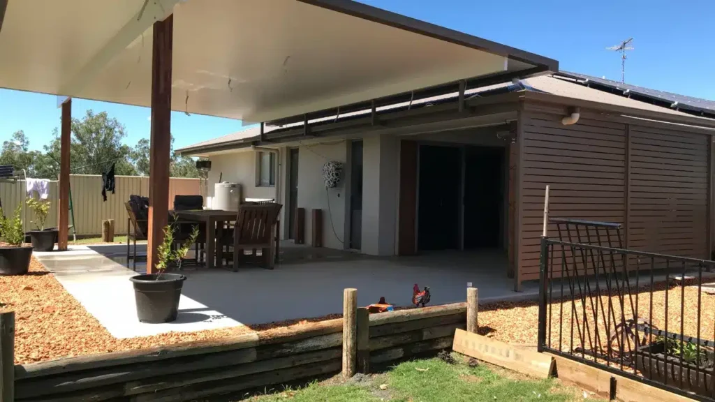 Flat insulated patio with timber-clad posts at Emerald, Queensland attached to a rendered home, over a concrete area with outdoor dining setting, beside a lawn and timber retaining wall